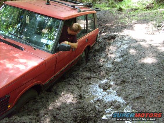 Red Range Rover stuck in mud, driver looking out window