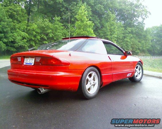 Red 1993 Ford Probe GT parked on wet asphalt, trees in background