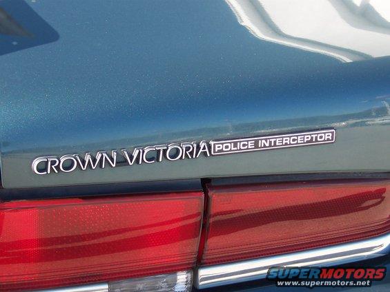 Crown Victoria Police Interceptor badge on a teal car's trunk lid, above a red taillight