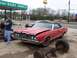 1972 Ford LTD - Red convertible with damaged hood parked outside a body shop. Parts of a rear axle are in the foreground.