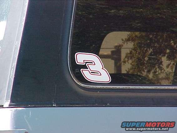 White number 3 sticker with red outline on dark tinted rear window of a vehicle
