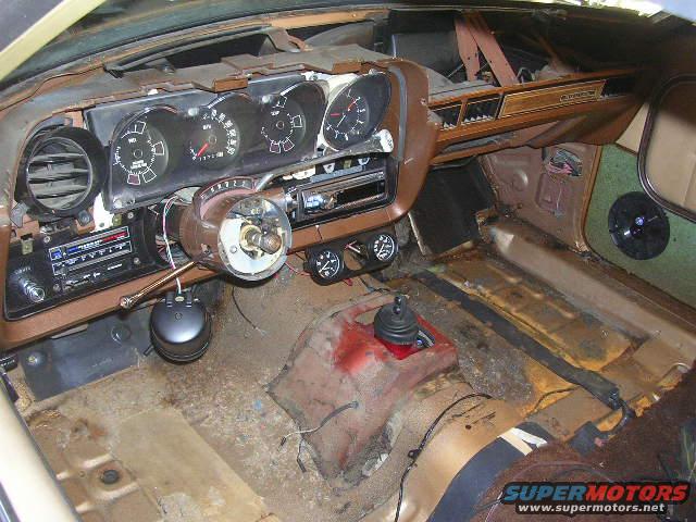 1975 Ford Ranchero interior showing dashboard, steering column, and floor. The interior is in a state of disassembly