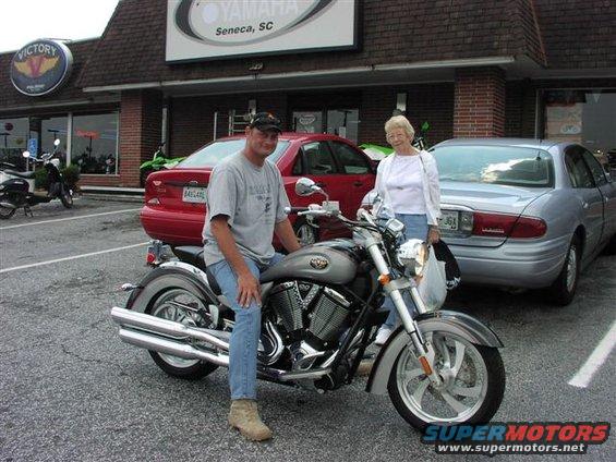 Silver Victory motorcycle with dual exhaust, parked in front of a dealership with a man seated on it