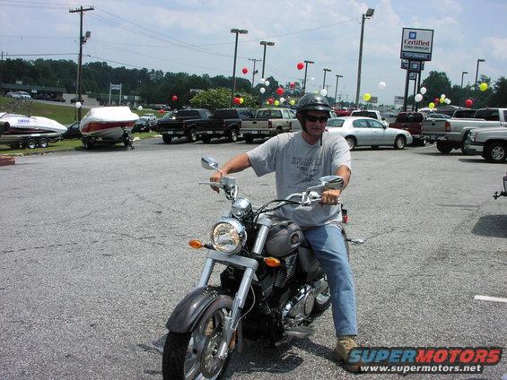 Man sits on a motorcycle in a parking lot with boats and trucks visible