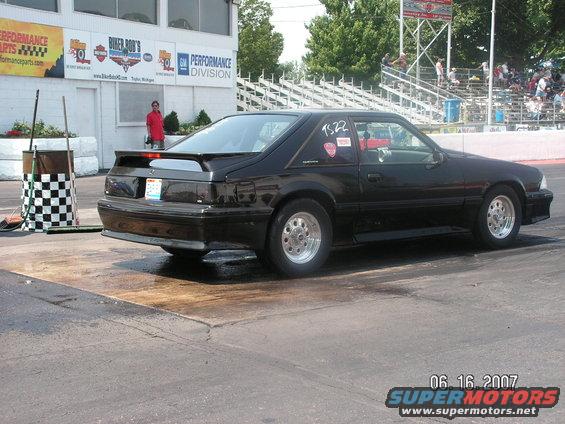 Black coupe with a spoiler and racing decals on the rear quarter panel, seen from the rear quarter angle