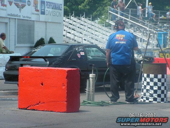 Black 1988 Ford Mustang with a spoiler and racing decals on the side, parked at a drag strip