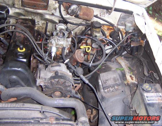 Engine bay with carburetor, alternator, and hoses. Some rust visible