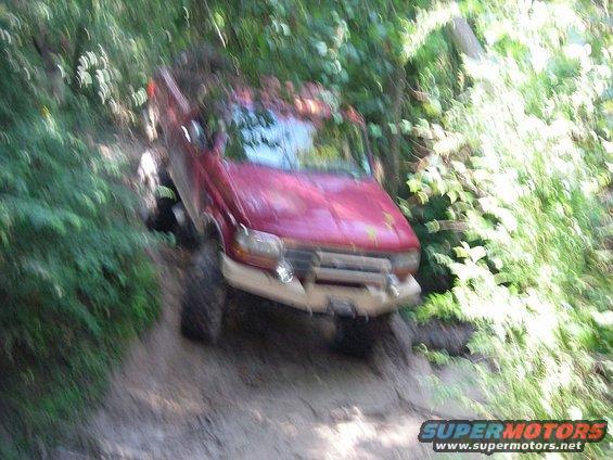 Red 1995 Ford Bronco navigating a steep, wooded trail