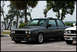 1989 BMW 3 Series - A dark gray coupe is parked in a lot next to another vehicle, with trees and buildings in the background.