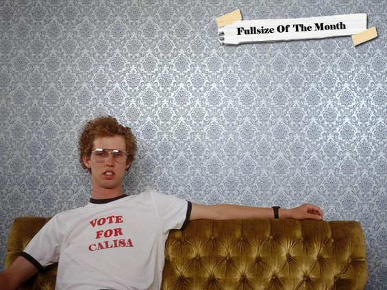Man with curly hair and glasses sits on a couch, wearing a white t-shirt with red text "VOTE FOR CALISA"