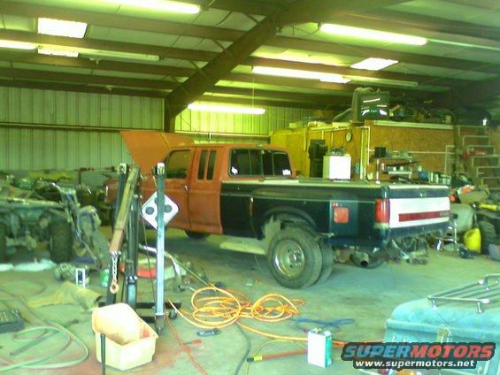 Ford F-Series dually truck with hood up, parked in a garage next to another vehicle. Appears to be undergoing repairs