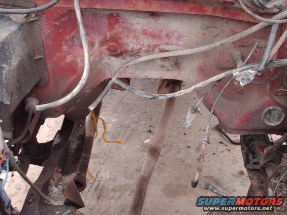 Red engine bay with visible rust and wiring. A metal pipe runs through the center