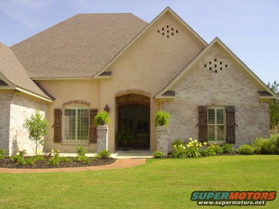 Front view of a house with light-colored brick and stucco, arched entryway, and shutters