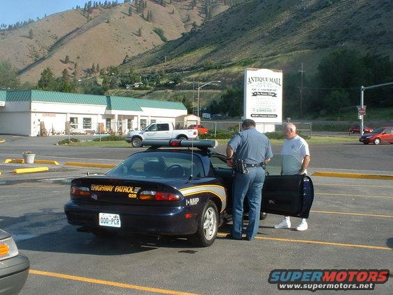 Dark blue police car with "HIGHWAY PATROL" text on rear, parked next to a white pickup truck