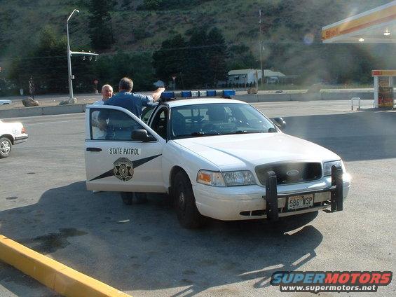 White Ford Crown Victoria police car with open driver's door, "STATE PATROL" text, and push bumper