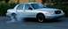 1998 Ford Crown Victoria - A silver sedan is performing a burnout, creating a cloud of smoke from its rear tires.