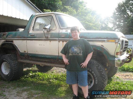 Boy standing in front of a two-tone green and white 1978 Ford Bronco with large tires