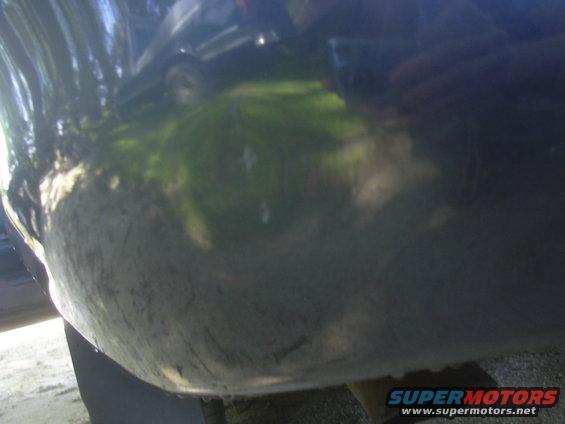 Reflection of a dark sedan on a dirty car bumper