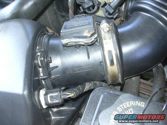 Close-up of a mass air flow sensor connected to a black intake tube, with visible wiring and a clamp