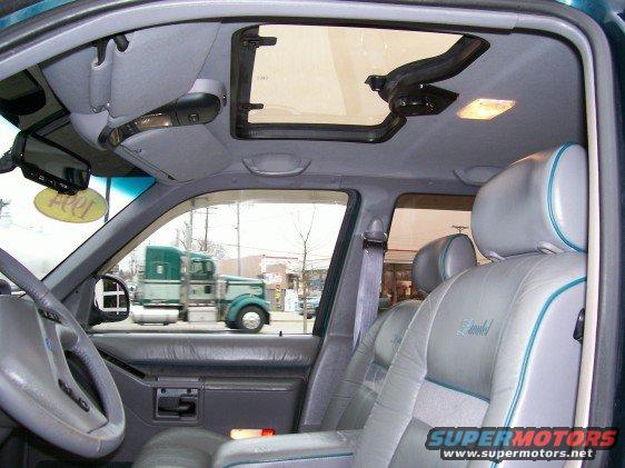 Interior shot of a 1994 Ford Explorer showing gray leather seats with teal trim, a sunroof, and two trucks visible through the window