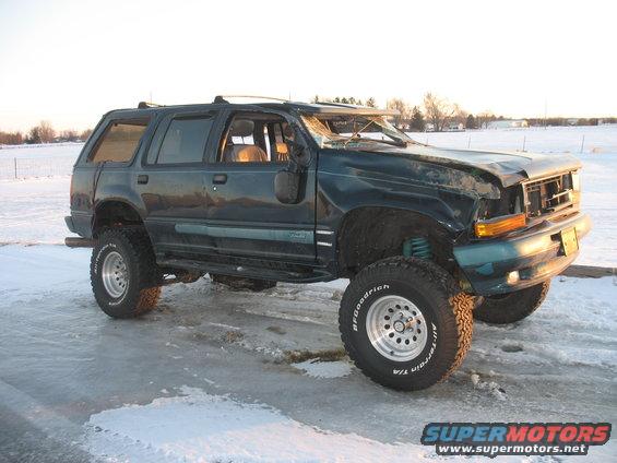 Dark green SUV with lifted suspension and damaged front end, parked on icy ground