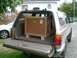 1995 Ford Probe - A tan SUV is parked with its tailgate open, revealing a large wooden crate secured inside. A second vehicle is partially visible to the lef…