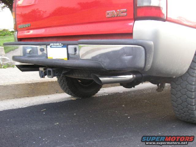 Rear view of a red GMC Sierra pickup truck showing the bumper, trailer hitch, and exhaust pipe. License plate is visible
