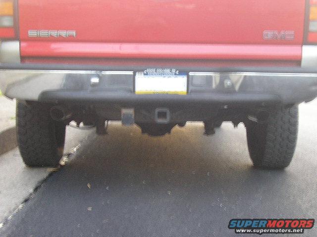 Red GMC Sierra pickup truck rear bumper with dual exhaust pipes and a trailer hitch