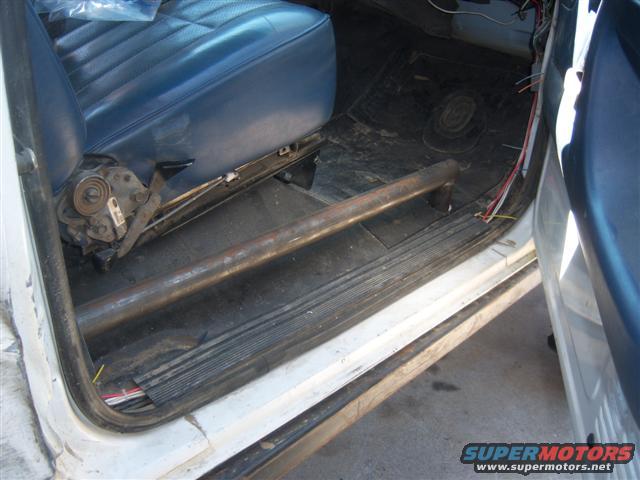 Interior view of a vehicle showing a blue seat, exposed wires, and a metal roll bar along the floor