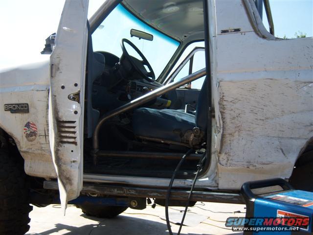 White 1995 Ford Bronco interior with rollcage, blue seats, and a welding machine outside