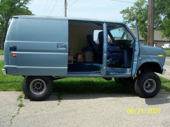 Blue van with sliding side door open and driver's door ajar, lifted suspension, aftermarket wheels