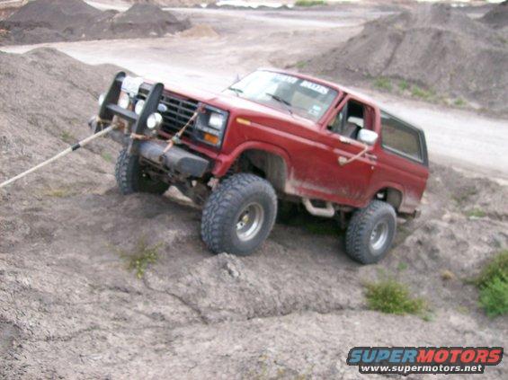 Red Ford Bronco with off-road tires climbing a dirt hill, winch cable attached to front bumper