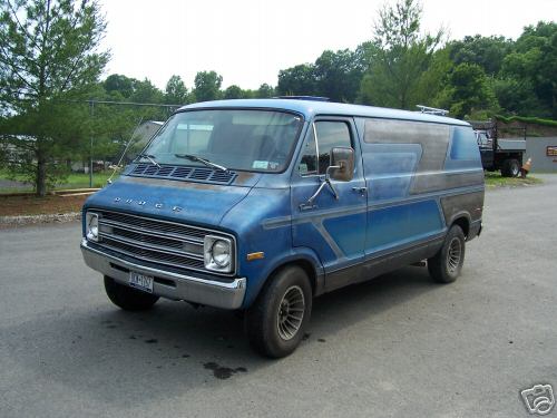 Blue 1977 Dodge van with custom side graphics and a roof rack, parked on asphalt