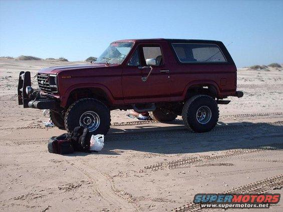Maroon Ford Bronco with aftermarket bumper parked on sand dunes