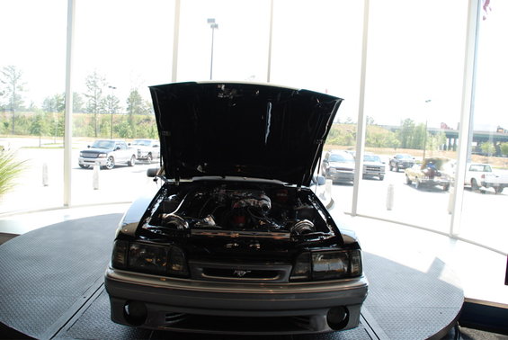 Black Ford Mustang with hood open, showing engine and twin turbos. Front view