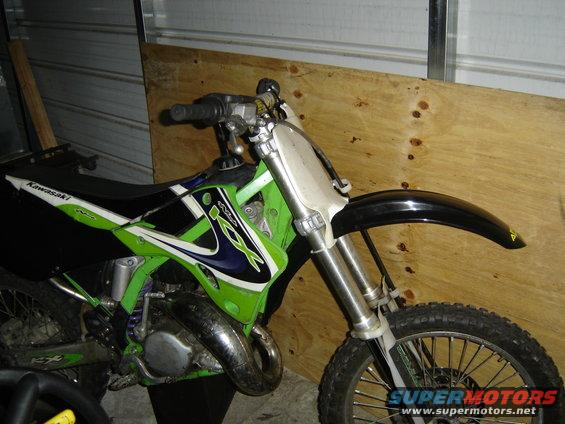 Green and black Kawasaki dirt bike, front wheel and handlebars visible, parked indoors