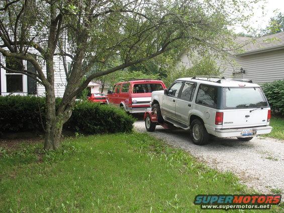 White 1995 Ford Explorer on a trailer, towed by a red truck
