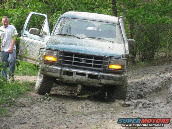 Teal Ford Bronco stuck in mud, driver's door open, snorkel visible