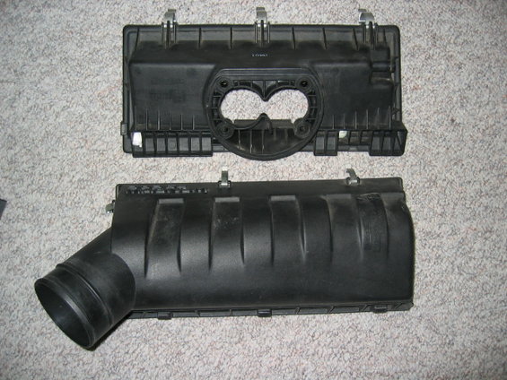 Two black plastic air cleaner housing components on a carpeted surface