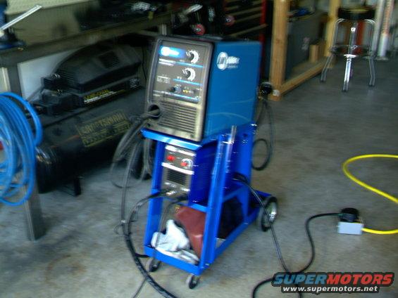 Miller welding machine on a blue cart next to a Craftsman air compressor