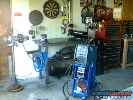 Welding machine on a cart, air compressor, and workbench in a garage
