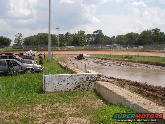 Mud bog with vehicles parked on the side and a vehicle in the mud