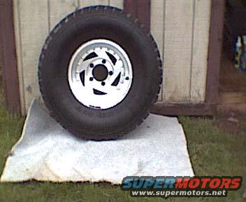 Tire and alloy wheel on white cloth in front of wooden wall