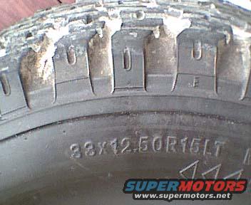 Close-up of a tire with text 33x12.50R15LT and SUPERMOTORS.NET logo