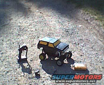 Remote control car, black and yellow, on gravel with a controller