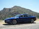 1995 Ford Probe - A blue 1995 Ford Probe is parked on a gravel road with a mountain landscape behind it.