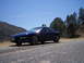 1995 Ford Probe - A blue 1995 Ford Probe is parked on the side of a road with trees and a hill in the background.