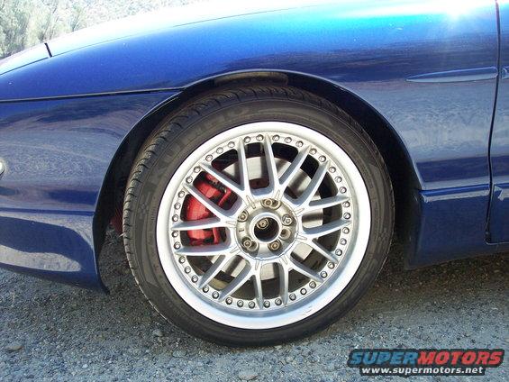 Blue car's front wheel with silver multi-spoke rim and red brake caliper
