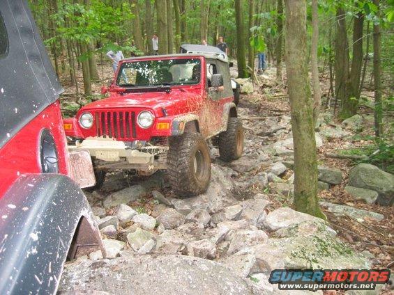 Red 2003 Jeep Wrangler navigating a rocky off-road trail with another Jeep partially visible on the left