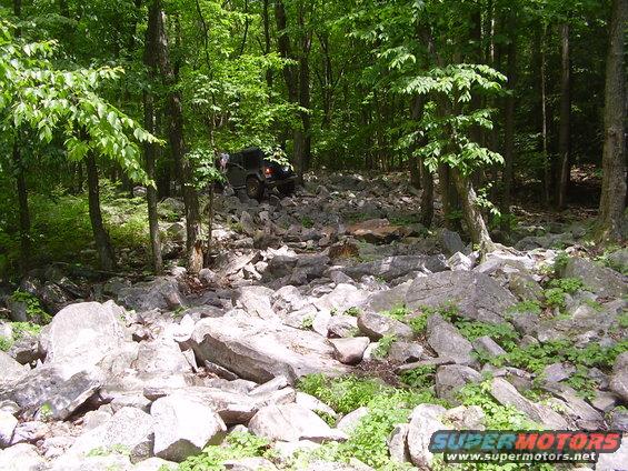2003 Jeep Wrangler navigating a rocky trail in a wooded area